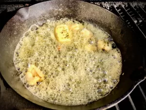 Garlic Butter melting in Cast Iron Skillet on a gas grill.