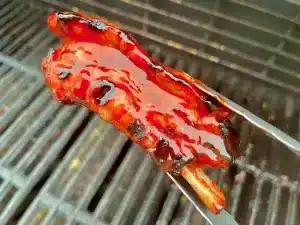 Grilled Pork Rib with Ah So sauce being held by some grilling tongs