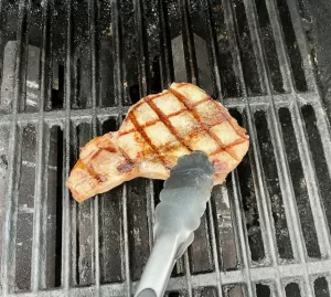 Grilling Tongs flipping a pork chop on a gas grill
