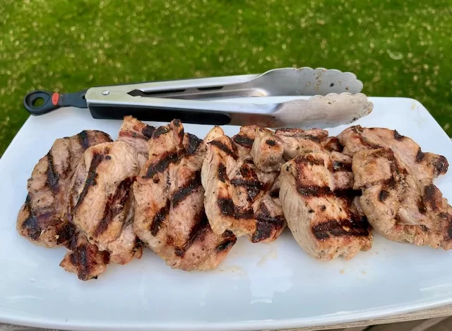 Pork Butt Steaks Plated with tongs and grass in the background.