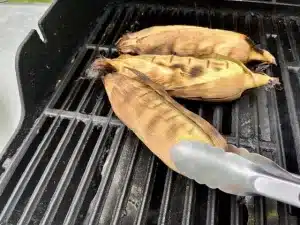 Tongs holding grilled corn