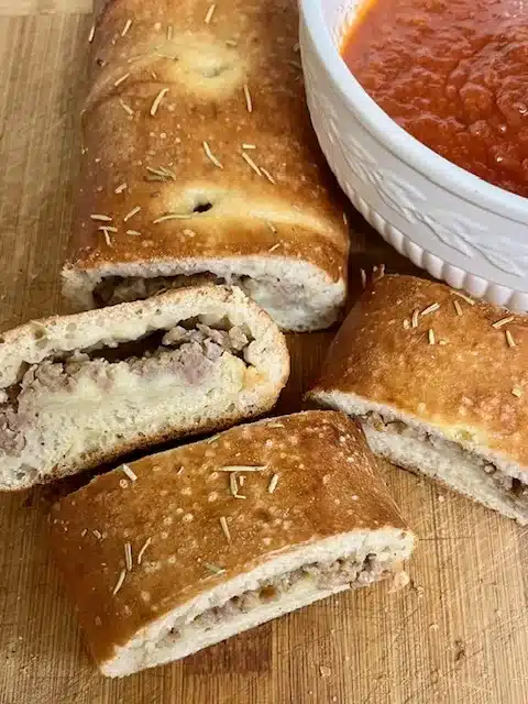 Grilled Sausage Bread sliced and sitting on cutting board with red sauce for dipping